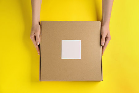 Woman holding cardboard box on yellow background, top viewの写真素材