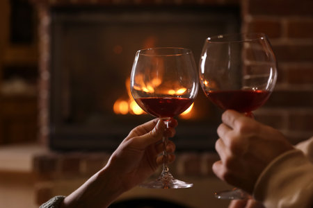 Lovely couple with glasses of wine near fireplace indoors, closeup. winter holidaysの写真素材