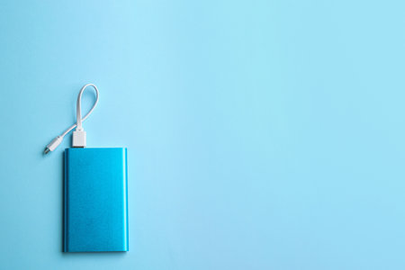Modern portable charger with cable on light blue background, top view. Space for textの写真素材