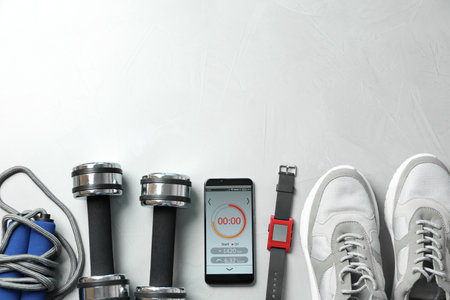 Smartphone with fitness app and sport accessories on white background, flat lay. Space for textの写真素材
