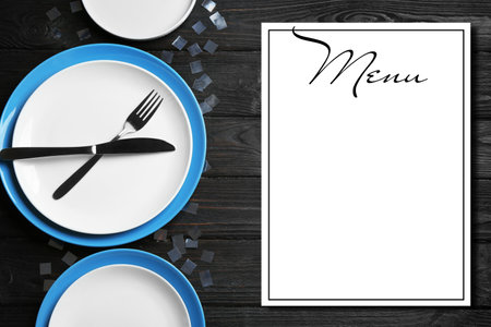 Elegant table setting and empty menu on black wooden background, flat lay. Space for textの写真素材