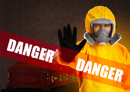 Funeral during virus pandemic. Man in protective suit near casket indoors