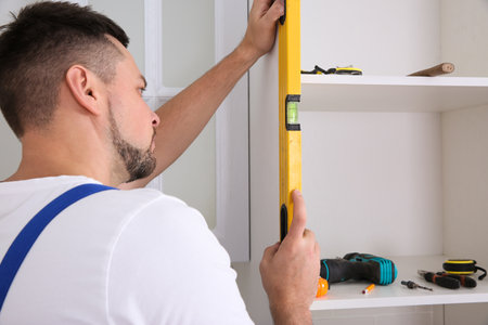 Worker measuring newly installed kitchen furniture indoors