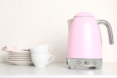 Modern electric kettle and dishes on counter in kitchenの写真素材