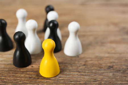 Yellow game piece among black and white ones on wooden background, closeup. Career promotion conceptの写真素材