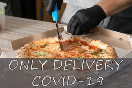Chef cutting oven baked pizza on table in restaurant, closeup. Online delivery service