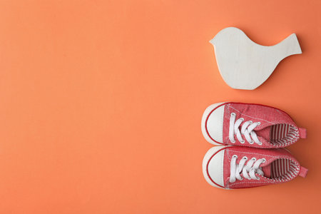 Child's shoes and wooden toy on coral background, flat lay with space for textの写真素材