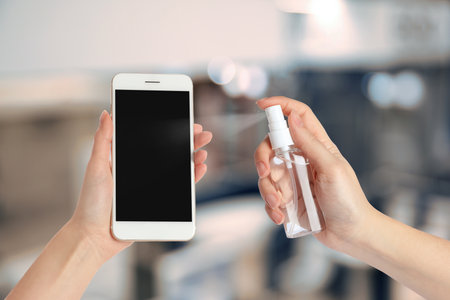 Woman sanitizing smartphone with antiseptic spray, closeup. Be safety during coronavirus outbreakの写真素材