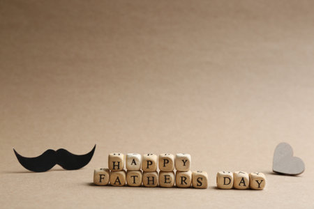 Words HAPPY FATHER'S DAY made with wooden cubes on beige background. Space for text