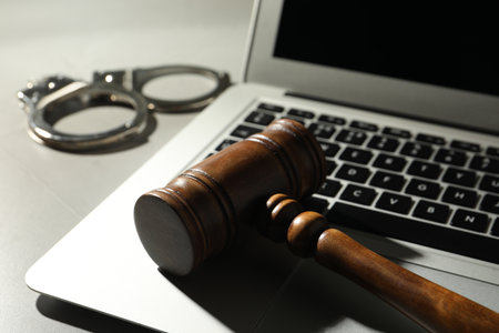 Laptop, wooden gavel and handcuffs on gray table, closeup. cybercrimeの写真素材