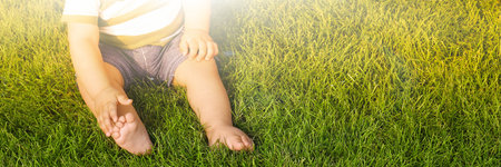 Adorable little baby sitting on green grass outdoors, space for text. banner designの写真素材