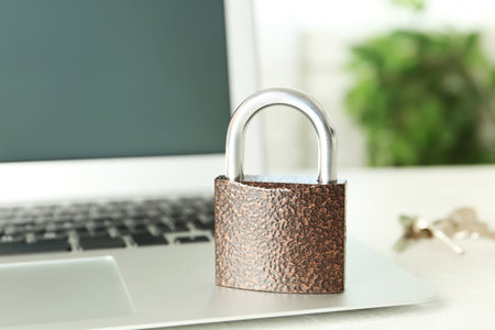 Metal lock and laptop on table, closeup. Protection from cyber attacks