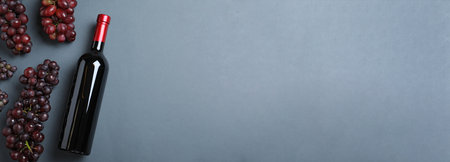 Fresh ripe juicy grapes and bottle of wine on gray background, flat lay with space for text. banner designの写真素材