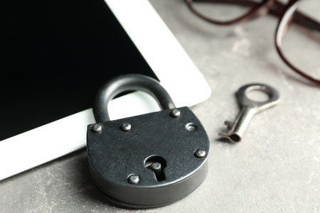 Vintage metal lock with key and tablet on gray table, closeup. Protection from cyber attacks