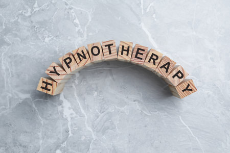 Wooden blocks with word HYPNOTHERAPY on light gray marble background, flat layの写真素材