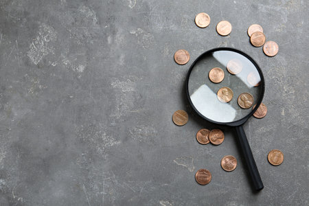 Magnifying glass and coins on gray stone table, flat lay with space for text. Search concept
