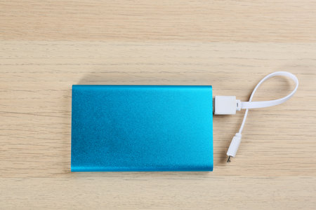 Modern portable charger with cable on wooden background, top viewの写真素材