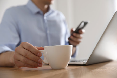 Man with cup of coffee at table indoors, closeupの写真素材