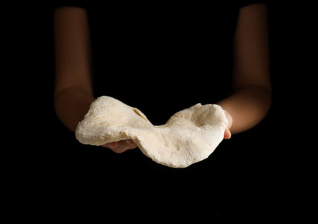 Woman preparing dough for pizza on black background, closeup