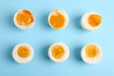 Different readiness stages of boiled chicken eggs on light blue background, flat layの写真素材
