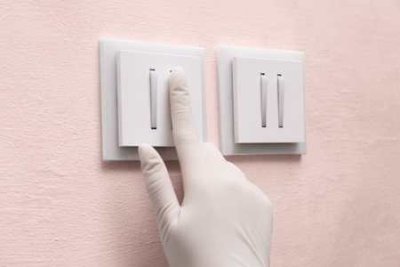 Woman in protective gloves pressing button of light switch indoors, closeup