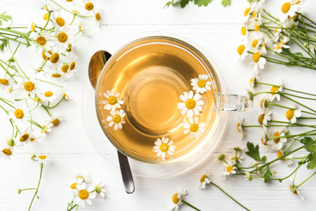 Flat lay composition with cup of tea and chamomile flowers on white wooden tableの写真素材