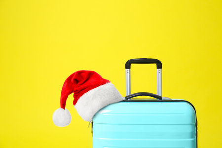 Stylish suitcase with Santa Claus hat on yellow background. christmas holidaysの写真素材