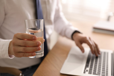 Office employee with glass of water at workplace, closeupの写真素材