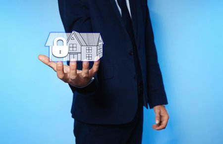 home security concept. Man holding house on light blue background, closeupの写真素材