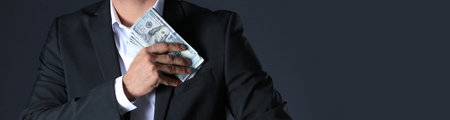 Man putting bribe into pocket on black background, closeup with space for text. banner designの写真素材