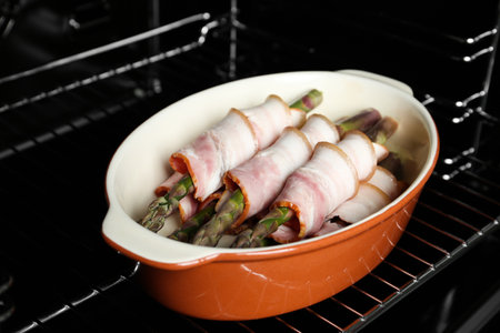 Uncooked bacon wrapped asparagus in baking dish on oven rack, closeupの写真素材