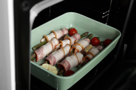 Uncooked bacon wrapped asparagus in baking dish on oven rack, closeupの写真素材