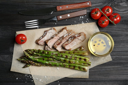 Tasty meat served with grilled asparagus on black wooden table, flat layの写真素材
