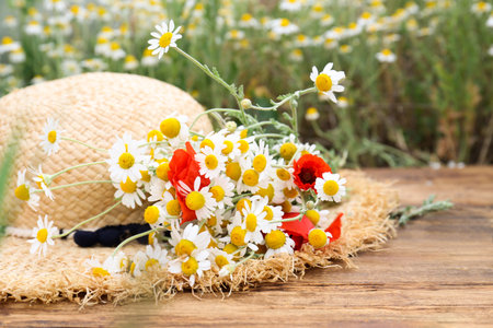 Bouquet of poppies and chamomiles with straw hat on wooden table outdoorsの写真素材