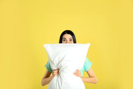 Young woman with pillow on yellow backgroundの写真素材