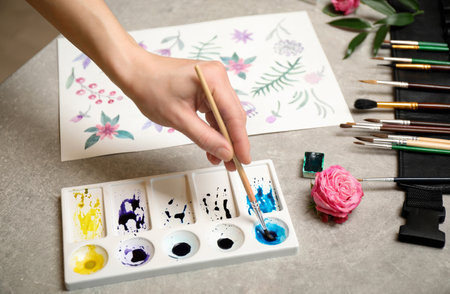 Woman painting flowers with watercolor at gray stone table, closeup