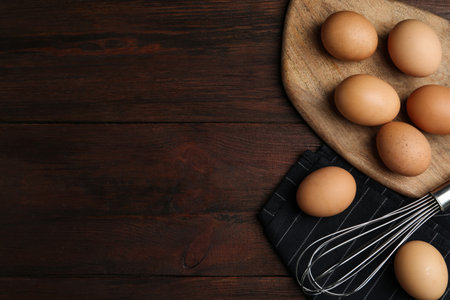 Chicken eggs and whisk on wooden table, flat lay. Space for textの写真素材