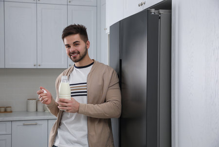 Young man with bottle of milk near refrigerator in kitchenの写真素材