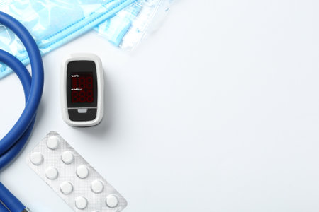 Flat lay composition with modern fingertip pulse oximeter and medical items on white background....