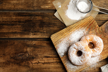 Delicious donuts with powdered sugar on wooden table, flat lay. Space for textの写真素材