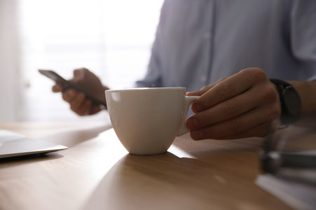 Man with cup of coffee at table indoors, closeupの写真素材