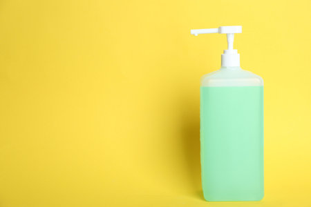 Dispenser bottle with green antiseptic gel on yellow background. Space for textの写真素材