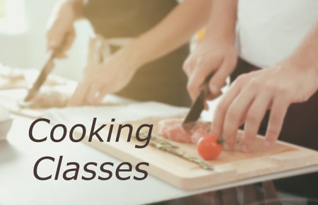 cooking classes. Blurred view of man cutting meat on wooden board at table, closeupの写真素材