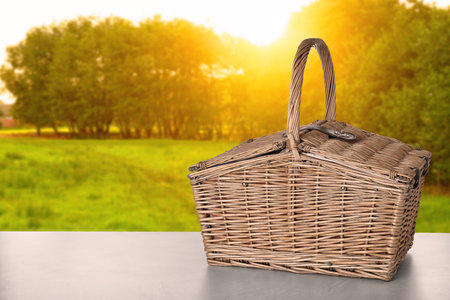 Wicker picnic basket on table in park, space for textの写真素材