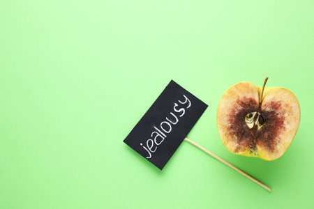 Rotten apple and JEALOUSY sign on green background, flat lay. Space for textの写真素材