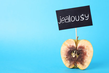 Rotten apple with JEALOUSY sign on light blue background. Space for textの写真素材