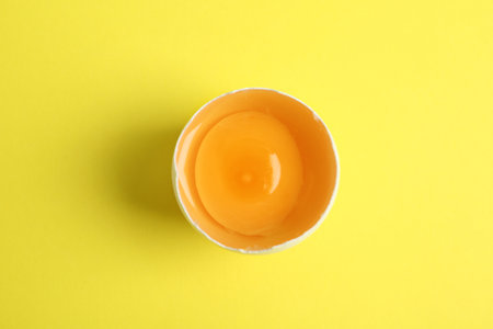 Broken raw chicken egg on yellow background, top viewの写真素材