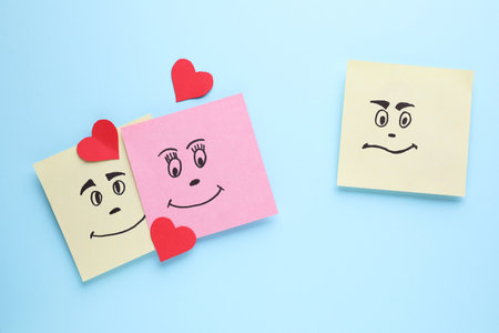 Paper notes with drawn faces on light blue background, flat lay. concept of jealousyの写真素材