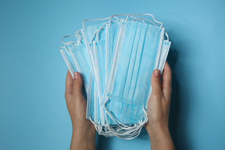 Woman holding disposable face masks on light blue background, closeup.