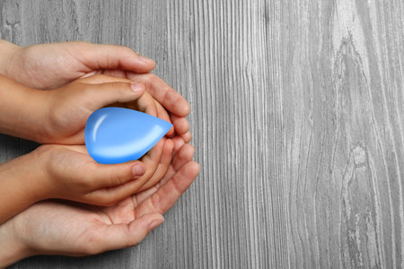 Woman and her child holding water drop on wooden background, top view with space for text. Ecology protectionの写真素材